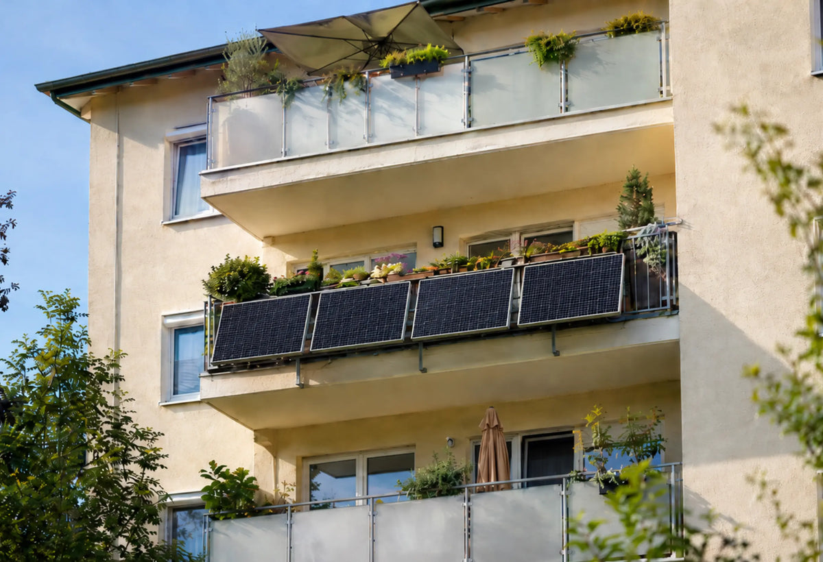 Wohnhaus mit bepflanzten Balkonen und vier gleich großen, leicht angewinkelten Solarmodulen am Balkongeländer als Beispiel für ein modernes Balkonkraftwerk.