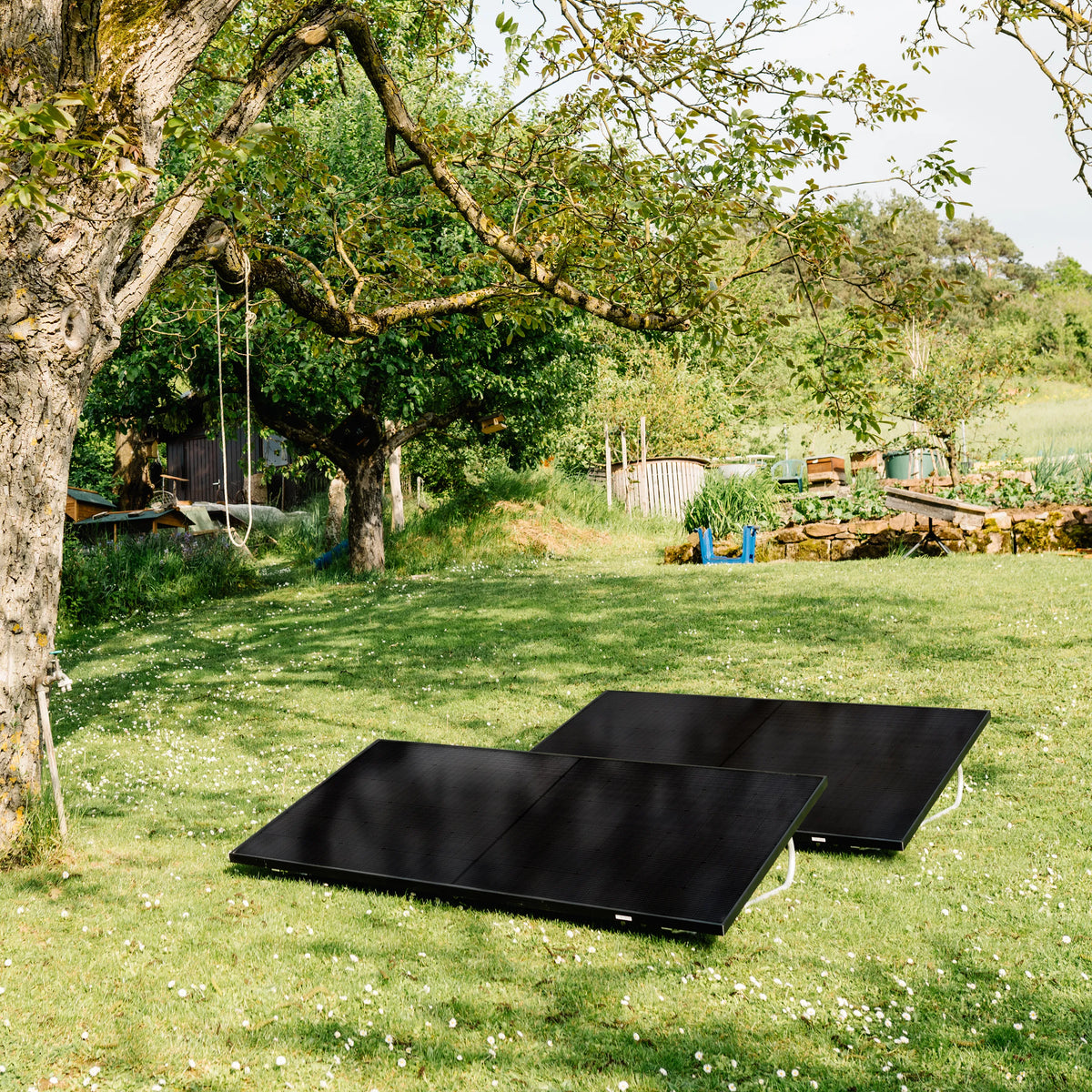 2 schwarze Solarmodule, die in einem Garten auf einer grünen Wiese aufgestellt sind